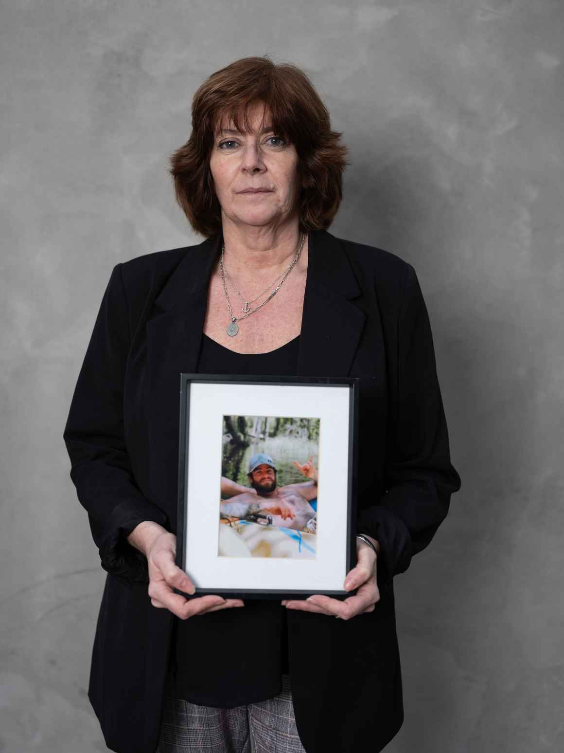 white woman in black blazer standing in front of a grey background holding a photo