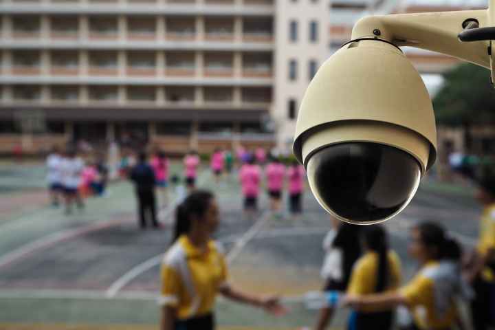 In the foreground, a security camera is situated against a background of students playing during recess