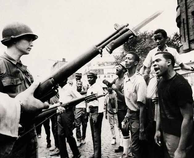 Photograph of Newarkers during the rebellion, who are facing national guard officers holding bayoneted guns.